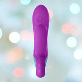 A purple Femme Funn Cora Rabbit Vibrator by Femme Funn is positioned vertically against a blurred background with multicolored bokeh lights. The toy features an intricately textured surface and a sleek design that promises powerful vibrations.